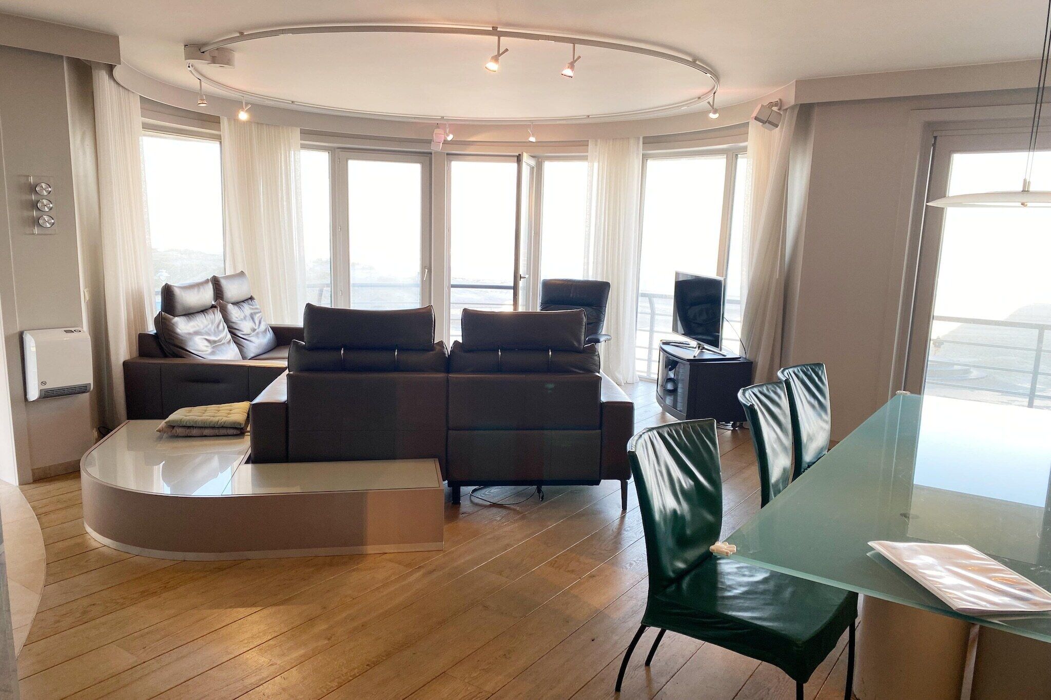 Uma sala de estar moderna com um sofá curvo, uma mesa de jantar de vidro e vista da cidade por grandes janelas.