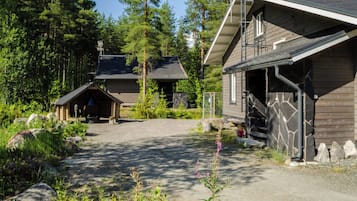 A cabin with a stone exterior, a wooden porch, and a gravel driveway surrounded by trees.