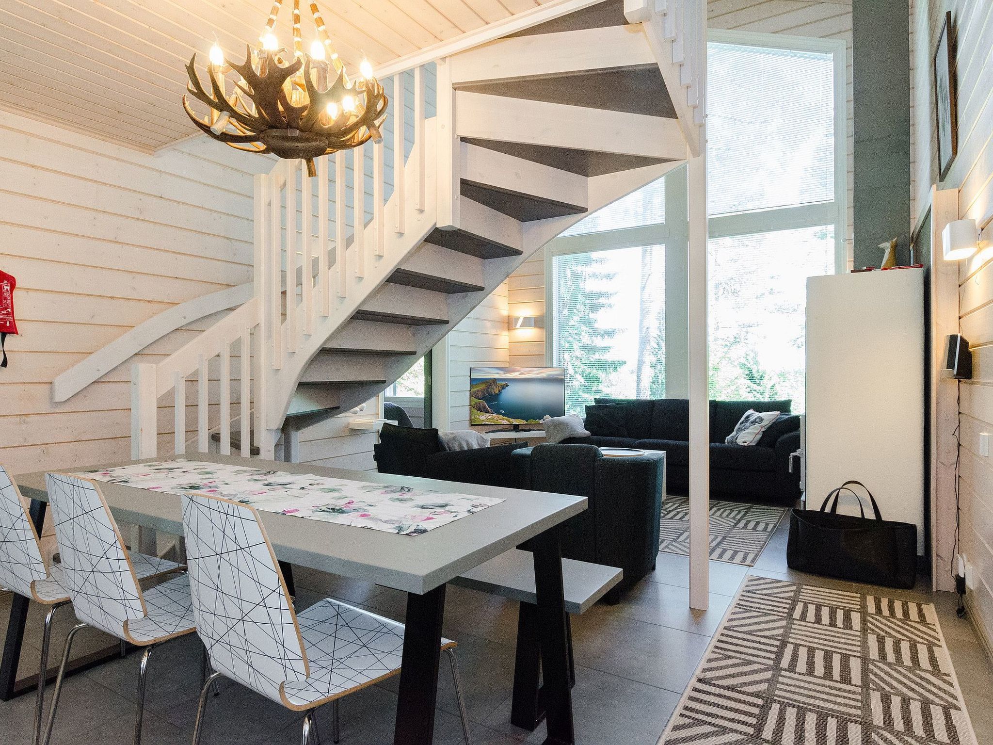 Un interior moderno con una escalera de caracol, una zona de comedor con mesa y sillas, y una sala de estar con sofá y televisión.