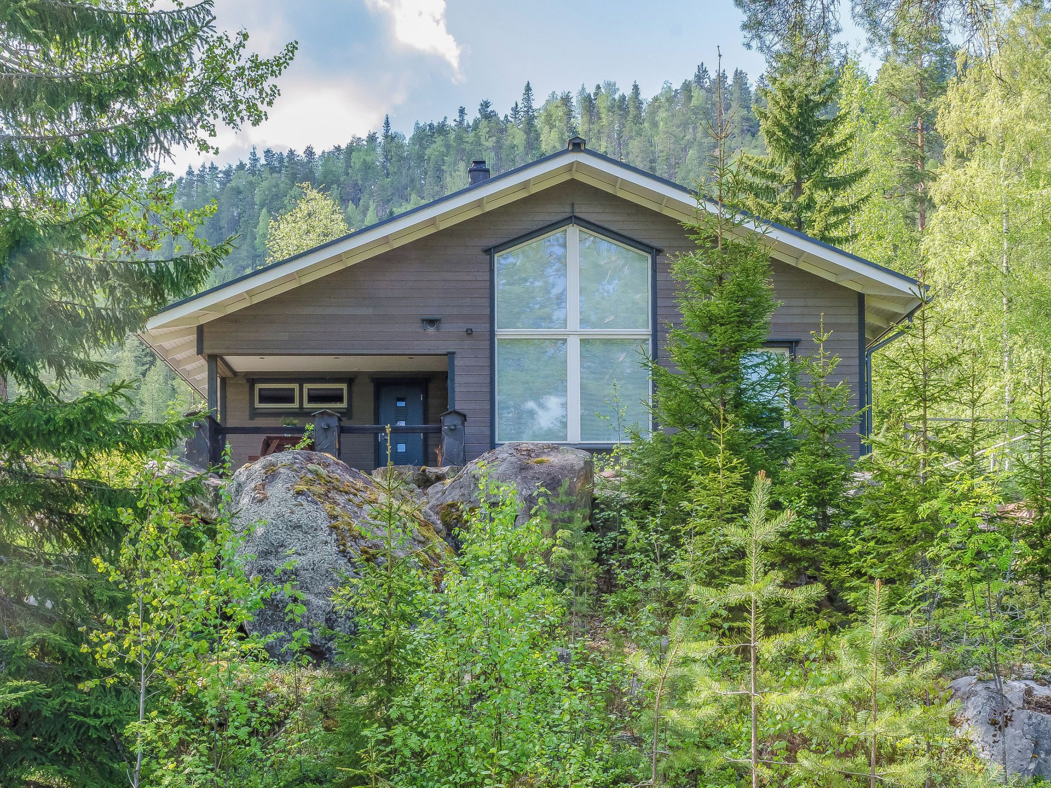 A modern house with a large window, surrounded by dense forest.