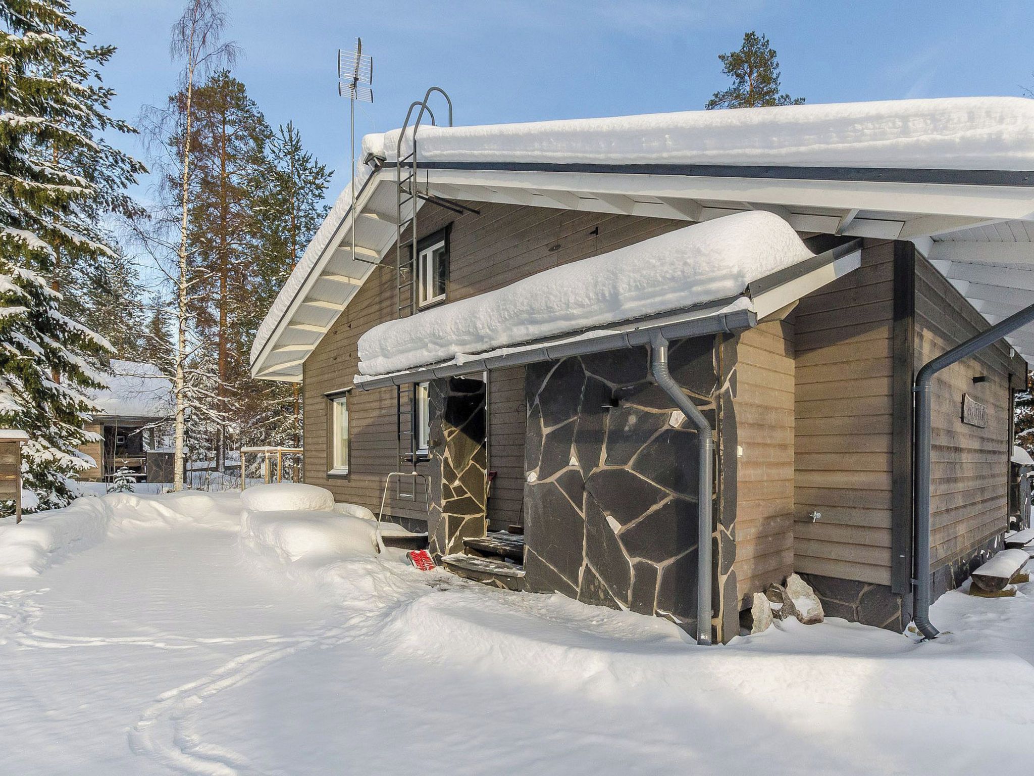 Una cabaña de madera con fachada de piedra, rodeada de nieve y árboles.