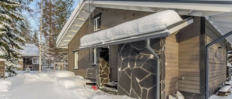 Una cabaña de madera con fachada de piedra, rodeada de nieve y árboles.