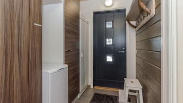 A narrow hallway with a dark door, a small white stool, and a white appliance on the left.
