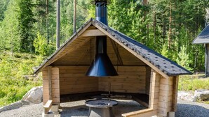 A wooden cabin with a chimney, a fire pit, and a gravel ground.