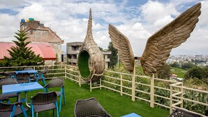 A rooftop terrace with wicker furniture, a unique green spiral structure, and large wing sculptures. - Paradise Hills Resort Hotel (Thaiba)