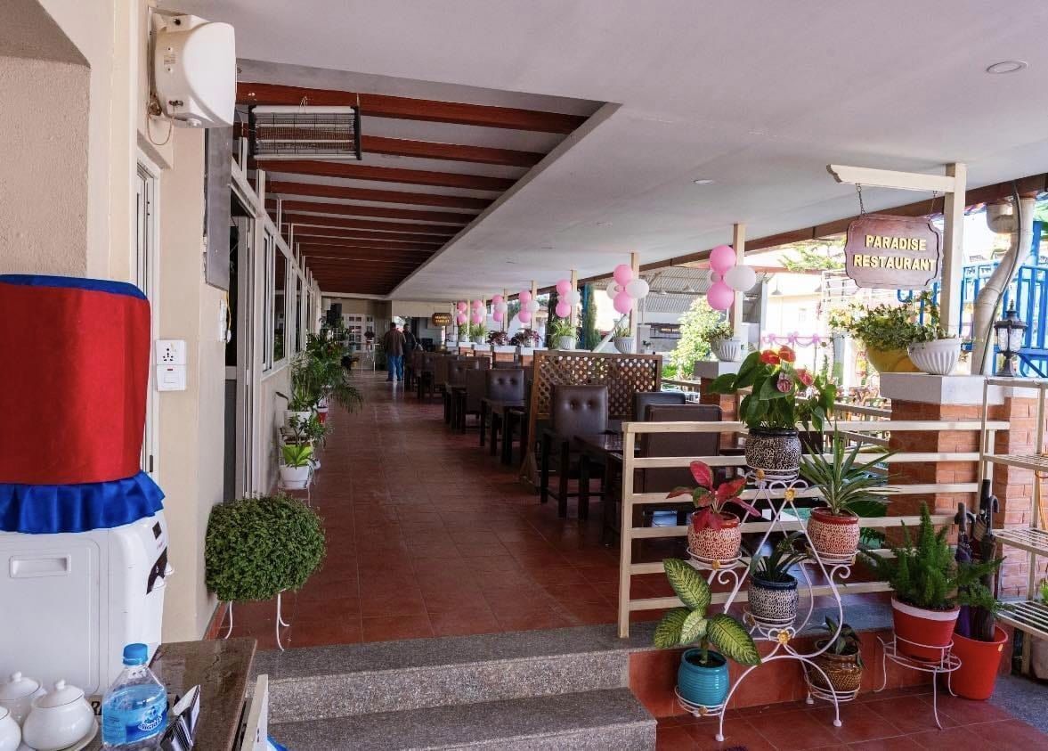 A restaurant with a covered outdoor seating area, potted plants, and a sign reading "Paradise Restaurant".