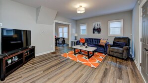 A living room with a TV, sofa, armchair, coffee table, and orange rug. - Chic Spacious Downtown Retreat (Indianapolis)