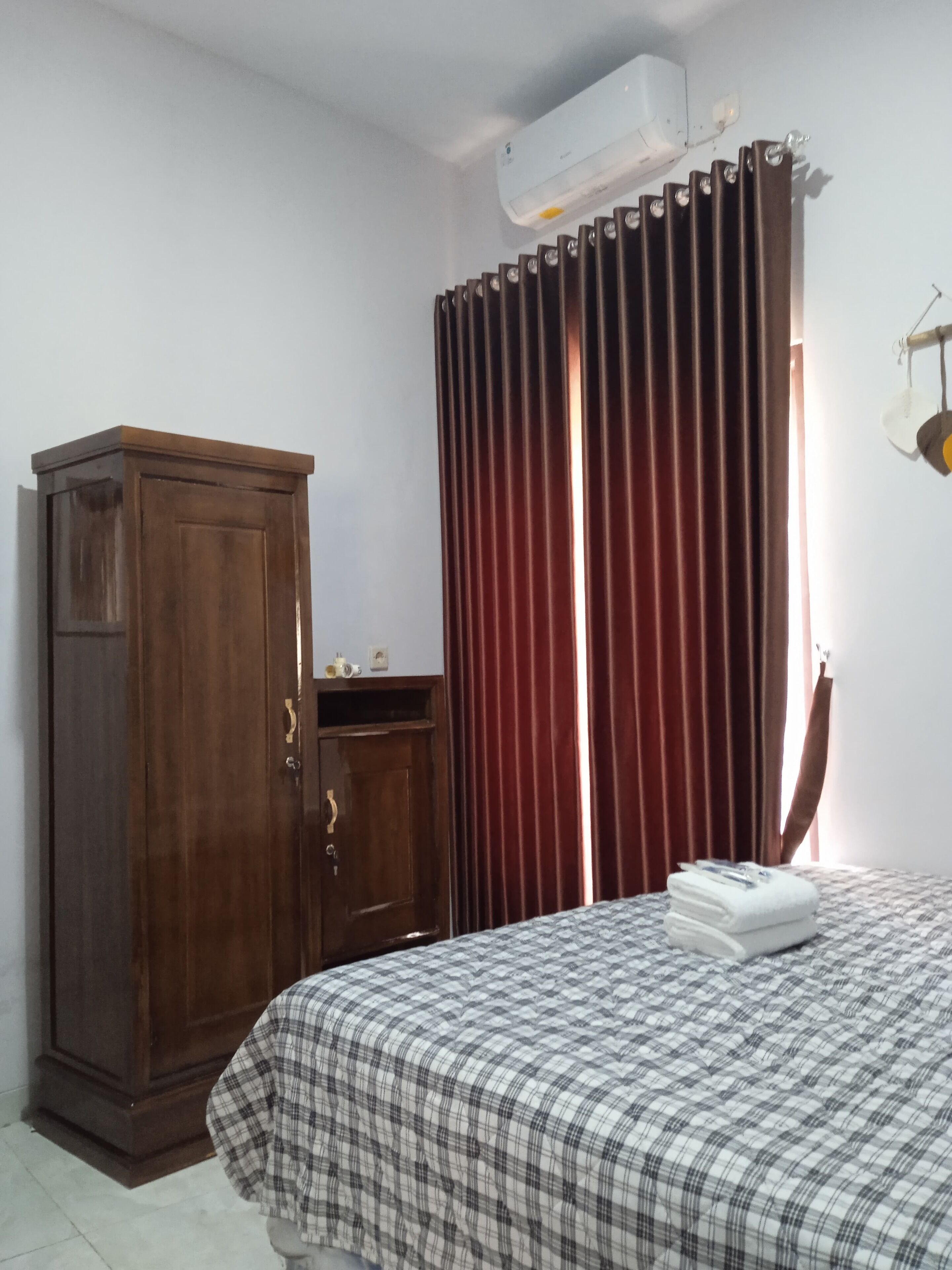 A bedroom with a bed, a wardrobe, a window with curtains, and an air conditioning unit.