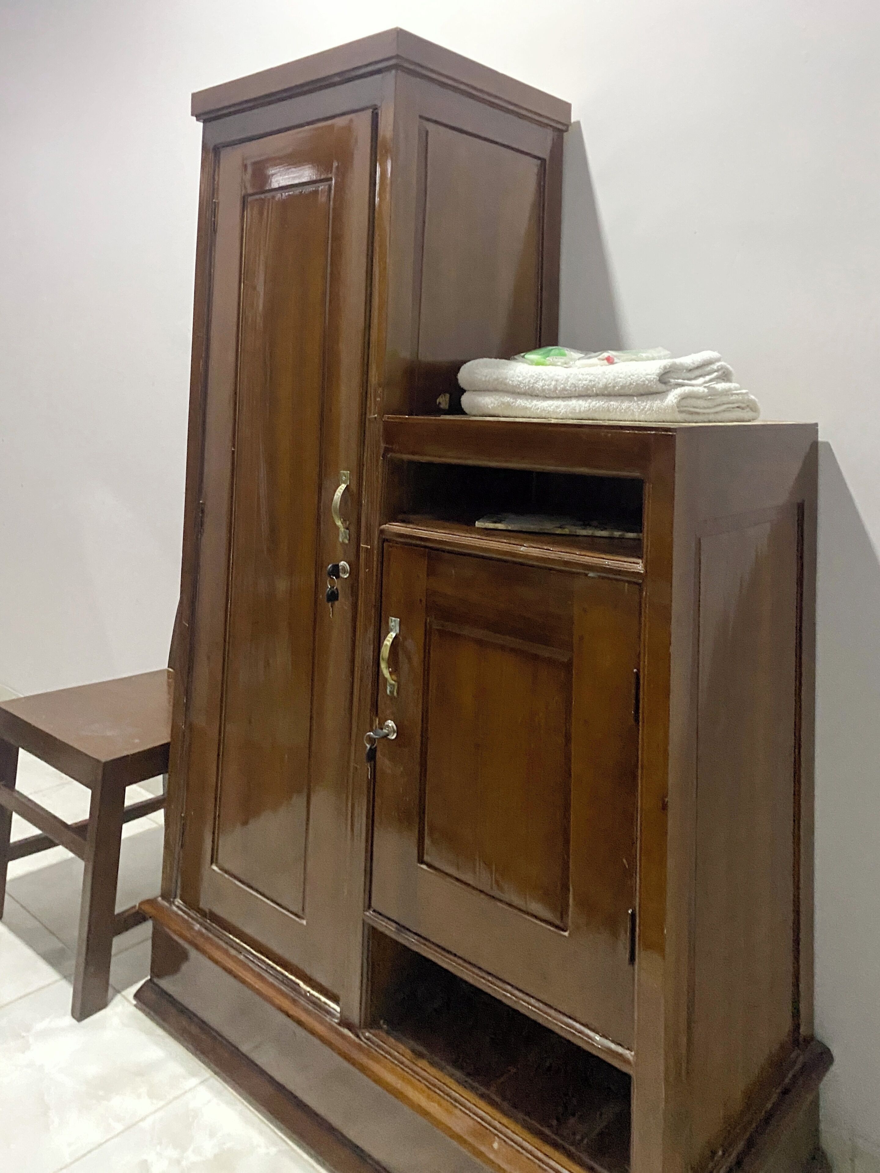 Un armario de madera con dos puertas y un estante, colocado contra una pared lisa.