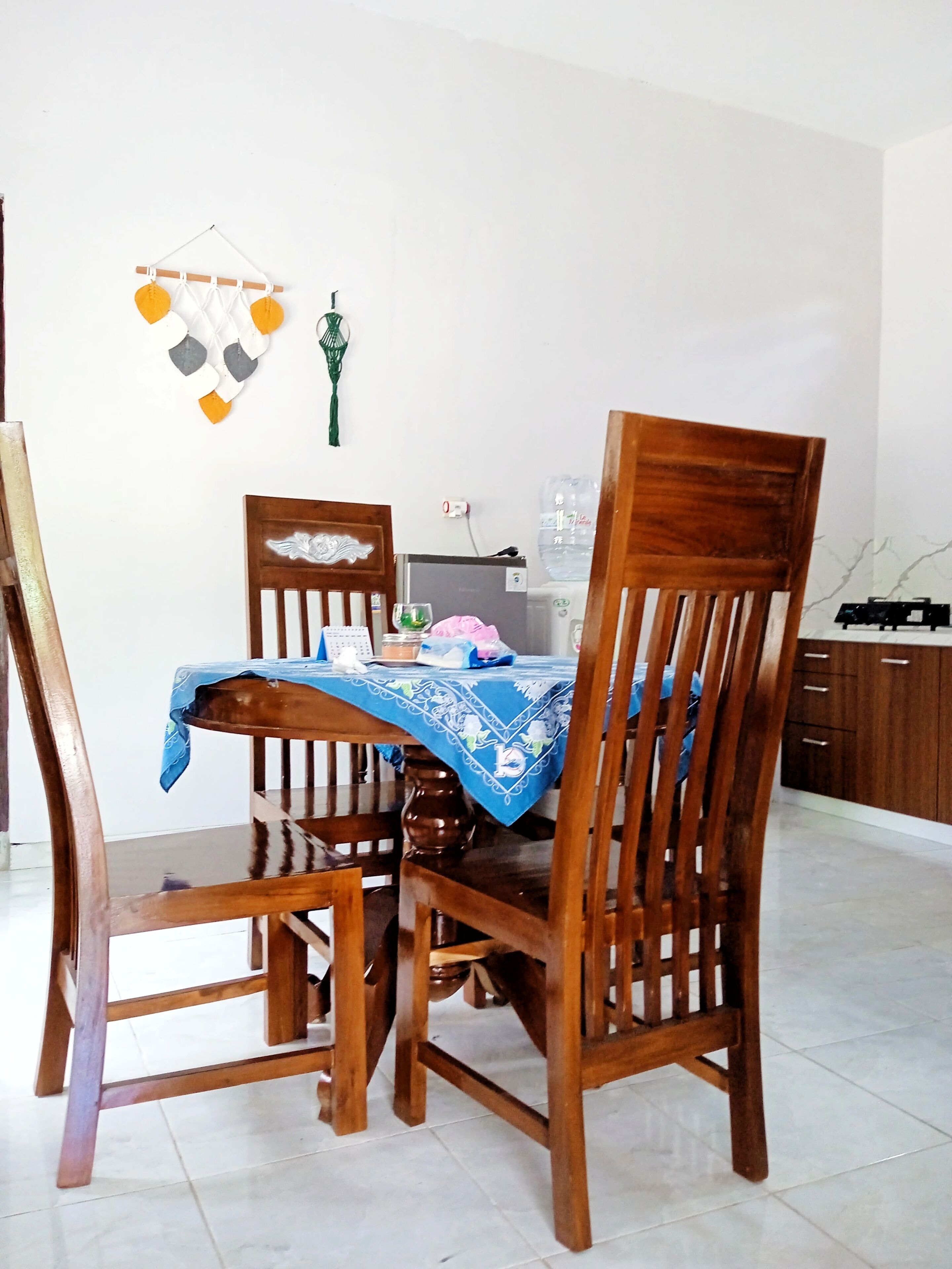 A dining area with a wooden table covered by a blue cloth, surrounded by wooden chairs.