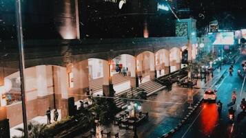 A nighttime view of Plaza Ambarrukmo with a modern architectural design, outdoor seating area, and a busy street with vehicles.