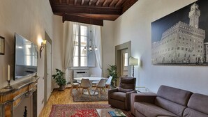 A living room with a fireplace, a dining area with a table and chairs, a brown leather sofa, and a large painting of a historic building. - Uffizi View (Firenze)