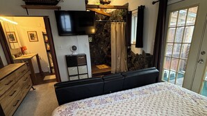 Ein Schlafzimmer mit einem großen Bett, einem an der Wand befestigten Fernseher, einer Steinwand und einem Fenster mit Vorhängen.