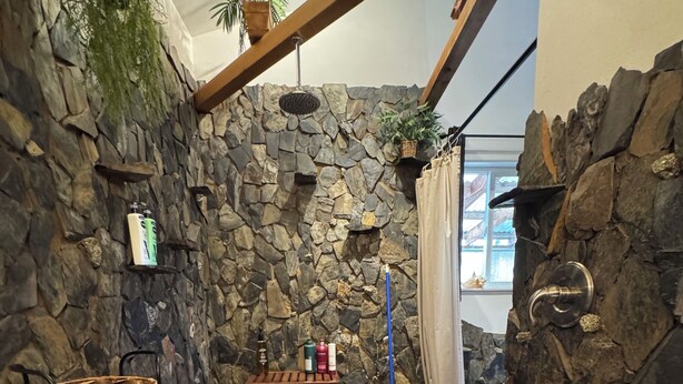 Ein Badezimmer mit Steinwand, einer Holzbank, einem kleinen Ablagefach mit Toilettenartikeln und einer weißen Badmatte.