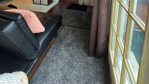 Ein gemütliches Wohnzimmer mit Kamin, einer schwarzen Ledersofa und einem großen Fenster mit Vorhängen.