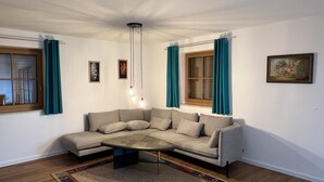 Una sala de estar moderna con un sofá gris en forma de L, una mesa redonda para café, cortinas color turquesa y un candelabro de techo.