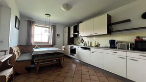 Cocina compacta con comedor, que incluye una banca y mesa, estufa, lavavajillas y diversos electrodomésticos.