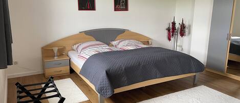 A modern bedroom with a wooden bed frame, striped pillows, a dark quilted bedspread, a bedside table with a lamp, and a small chair.