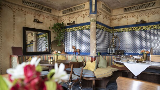 Un restaurante con pared de baldosas con diseño, un espejo y una zona de estar con mesas y sillas.