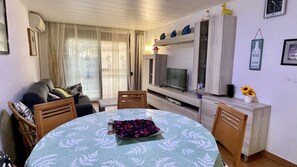 Ein Wohnzimmer mit rundem Tisch, einer Couch, einem Fernseher und einer Kommode mit Dekoration.