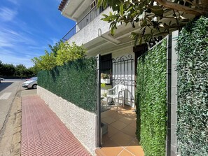 Um edifício residencial com portão fechado, calçada pavimentada e sebe verde.
