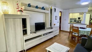 Ein Wohnzimmer mit Fernseher, einer Holzkommode und einem Essbereich mit Stühlen und Tisch.