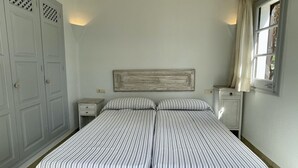 Ein Schlafzimmer mit zwei Einzelbetten, einem Kleiderschrank, einem kleinen Nachttisch und einem Fenster mit Vorhängen.