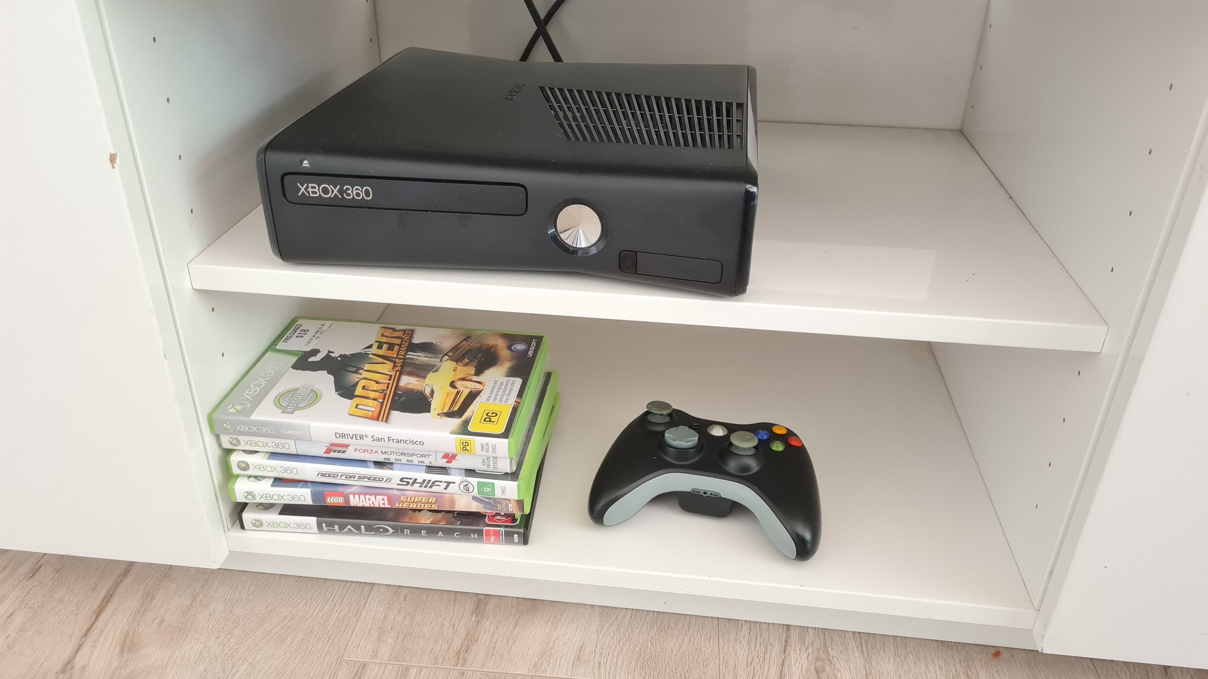 A shelf with an Xbox 360 console, a game controller, and several Xbox 360 games.