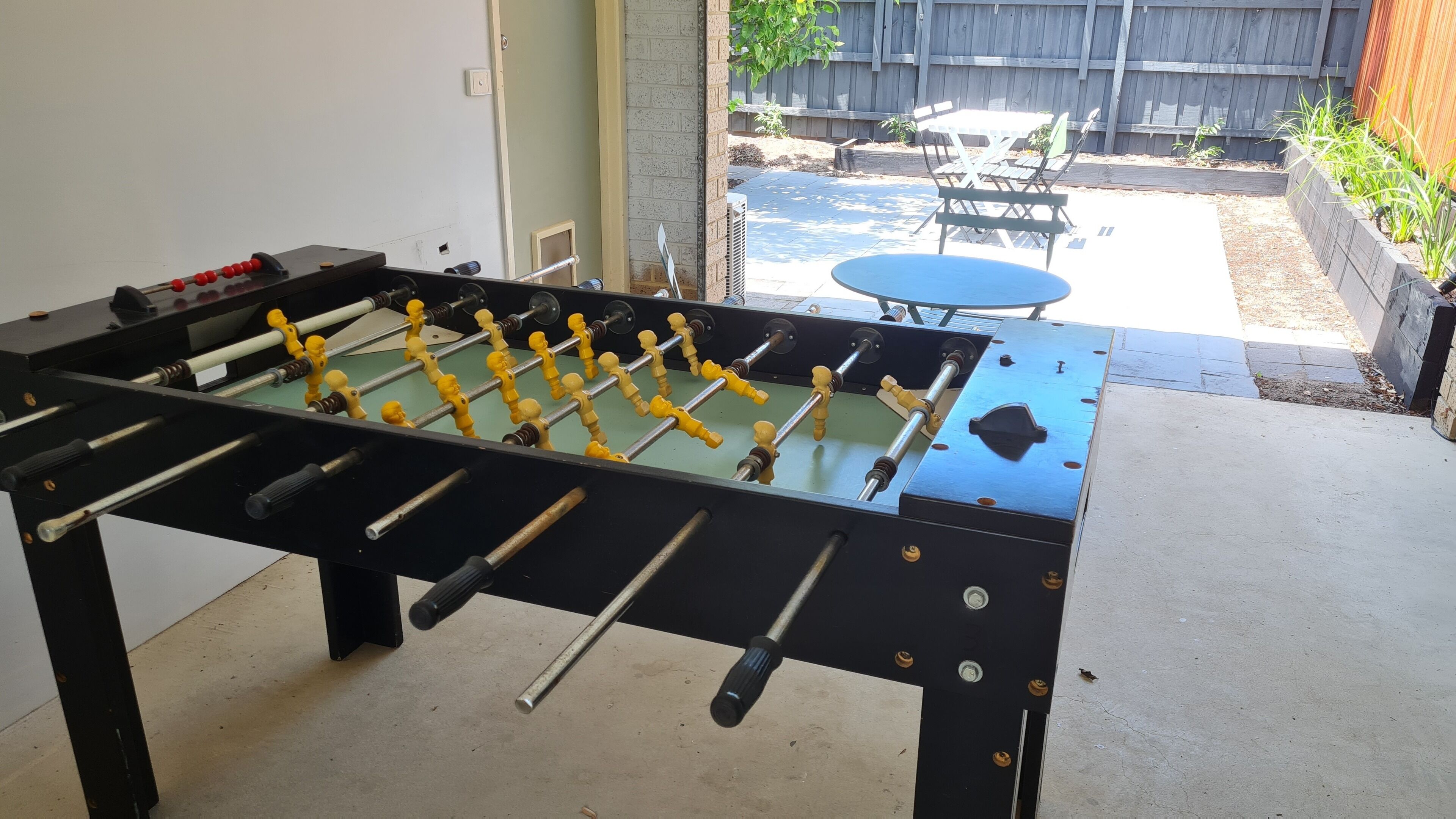 A foosball table in an outdoor patio area with a table and chairs in the background.