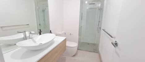 A modern bathroom with a large white sink, a toilet, and a glass-enclosed shower area.