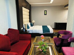 A modern hotel room with a large bed, red and purple seating, a glass coffee table with flowers, and a small desk. - HOTEL BILLIONS AIRPORT  (New Delhi)