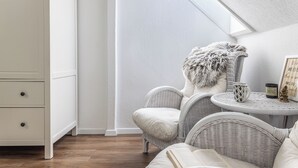 Quarto com guarda-roupa branco, cadeiras de vime, mesa redonda com uma vela e uma moldura com uma frase.