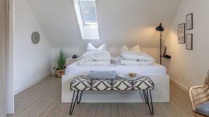 Quarto com cama, luminária de cabeceira, relógio na parede, janela e uma pequena planta.