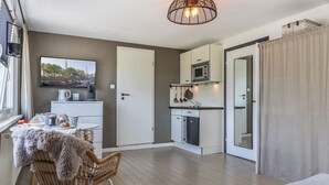 Um espaço de estar compacto com cozinha compacta, área de jantar com mesa e cadeiras, e um canto acolhedor com uma poltrona e um cobertor.