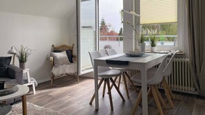 Ein moderner Essbereich mit einem weißen Tisch und Stühlen, ein Korbstuhl mit Felldecke und Blick ins Freie durch große Fenster.