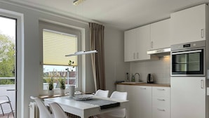 Eine moderne Küche mit weißen Schränken, einem eingebauten Backofen und einem Essbereich mit weißen Stühlen und einem Tisch.