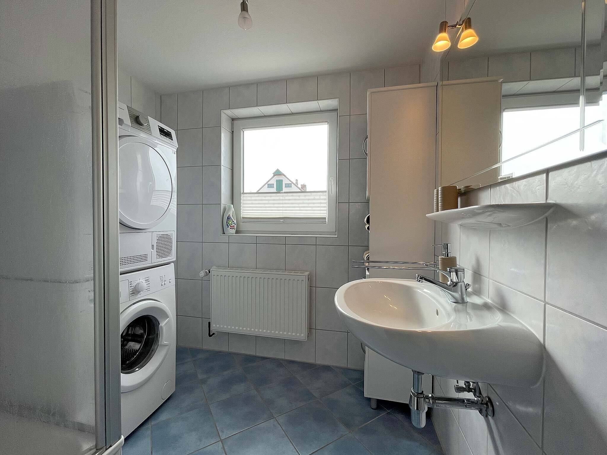 A compact bathroom with a washing machine, a sink, and a window with blinds.