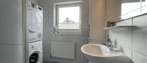 A compact bathroom with a washing machine, a sink, and a window with blinds.