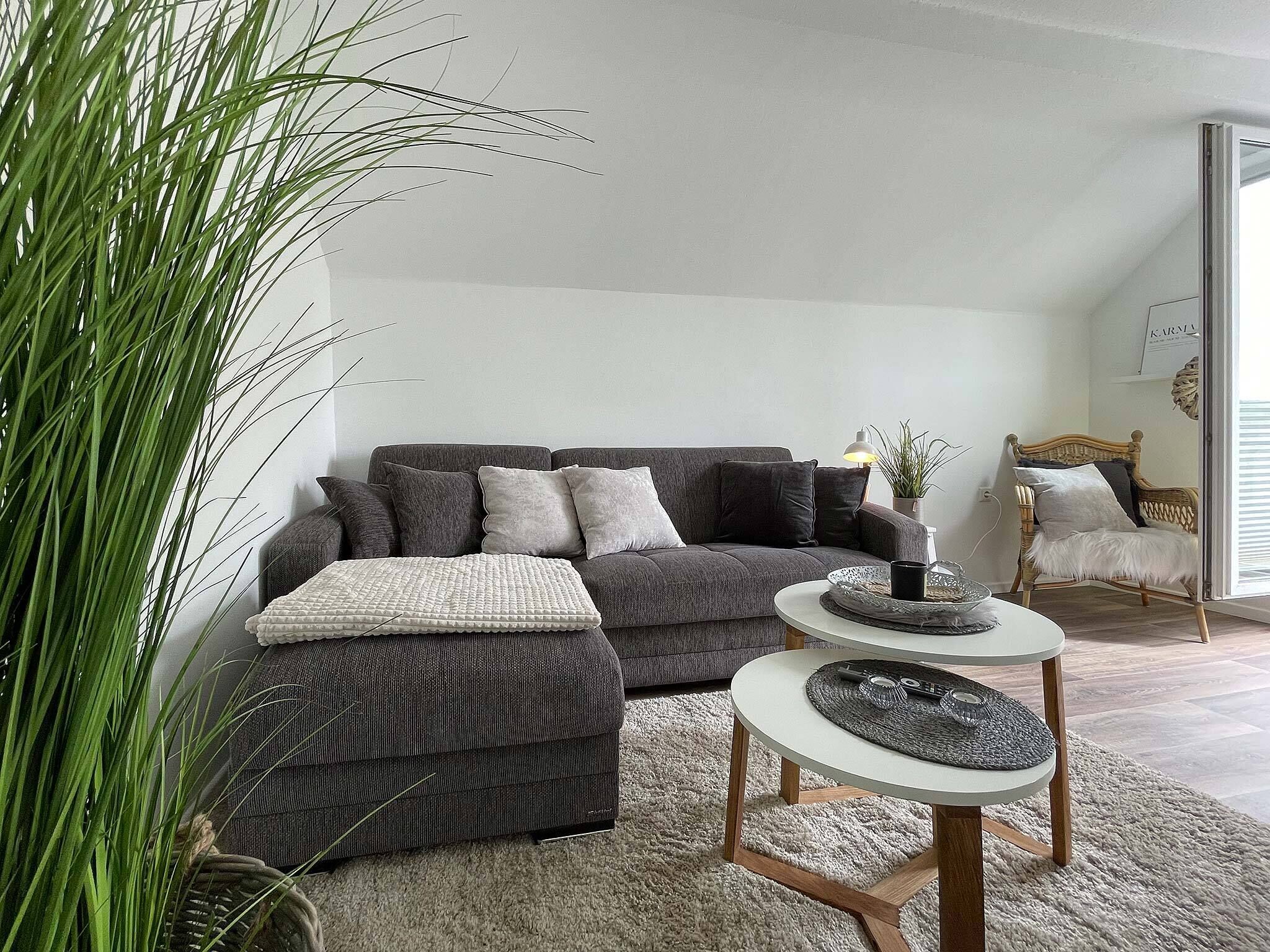 Una sala de estar moderna con un sofá gris, una mesa de centro redonda y una planta grande en maceta.