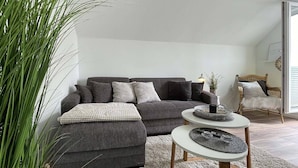 Ein modernes Wohnzimmer mit einem grauen Sofa, einem runden Couchtisch und einer großen Pflanze in einem Topf.