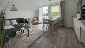 Ein modernes Wohnzimmer mit grauem Sofa, einem Esstisch und einer Küchenzeile mit Herd und Schränken.