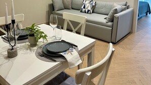 Un coin repas avec une table dressée pour deux personnes, un canapé gris et des tableaux encadrés au mur.