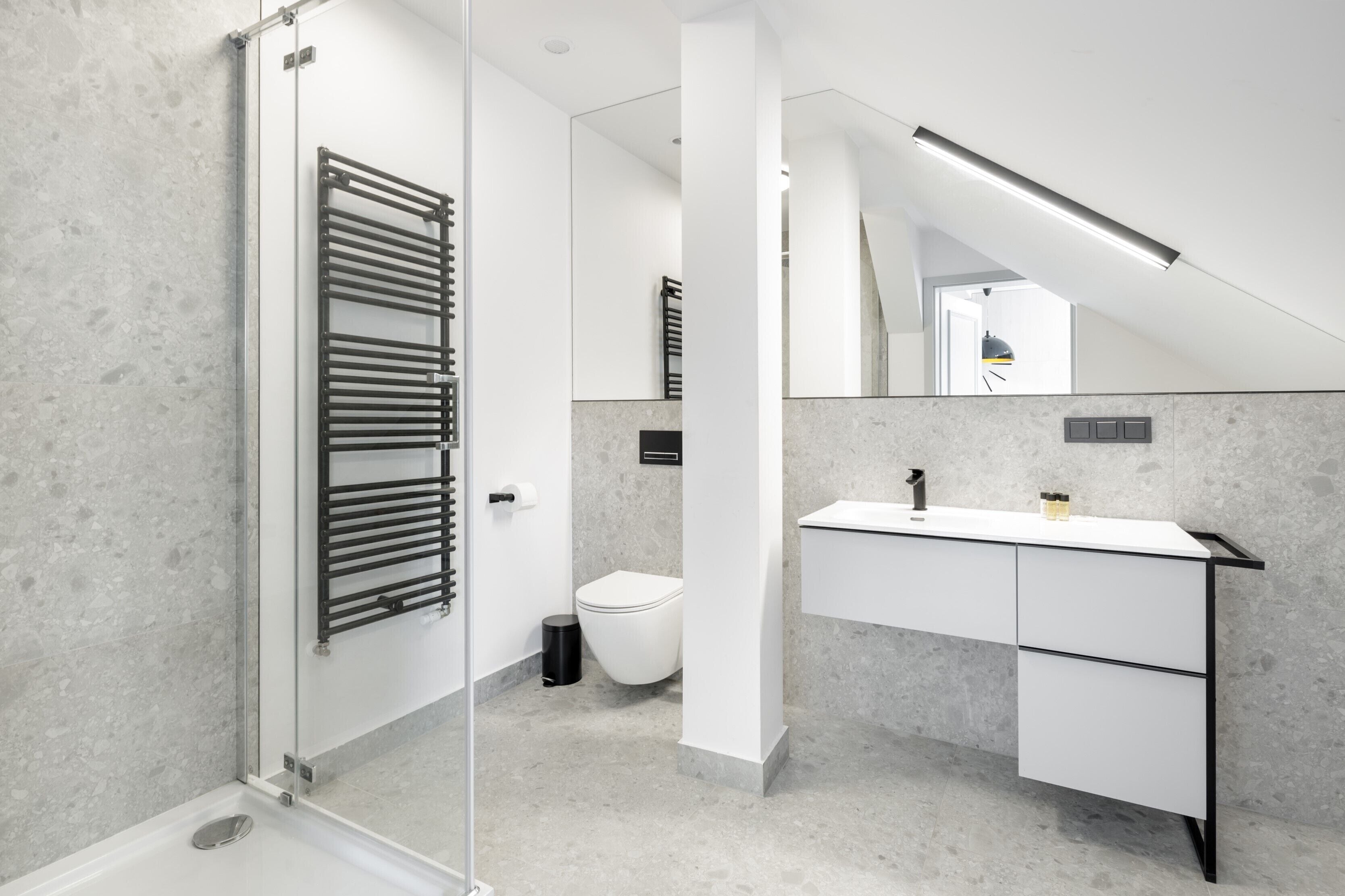 A modern bathroom with a glass shower enclosure, a white sink with a black countertop, and a large mirror above the sink.