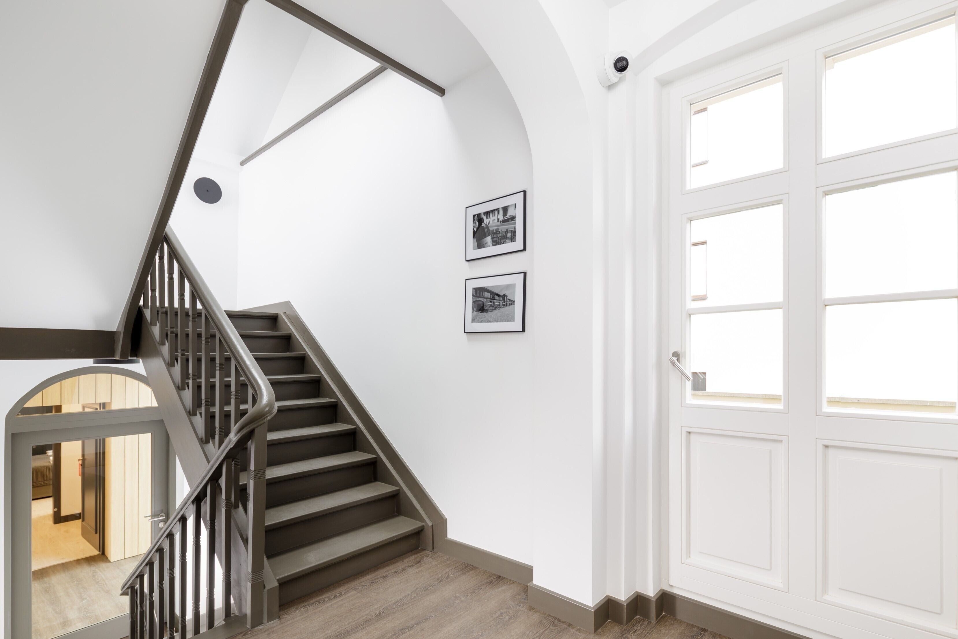 A staircase with a wooden finish, white walls, and two framed pictures.