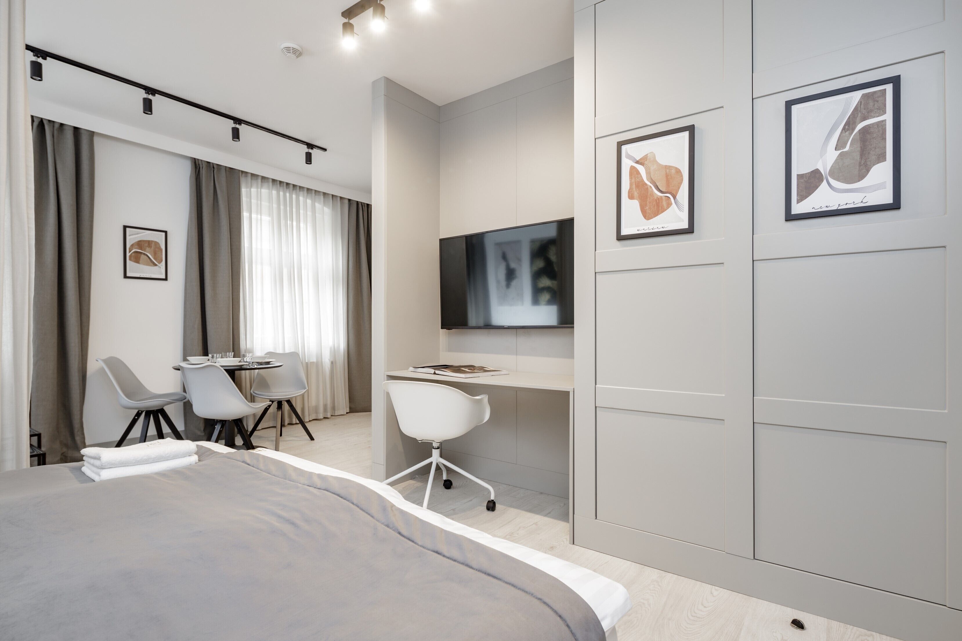 Una camera d'albergo moderna con un letto grande, una scrivania con una sedia, un televisore e opere d'arte alle pareti.