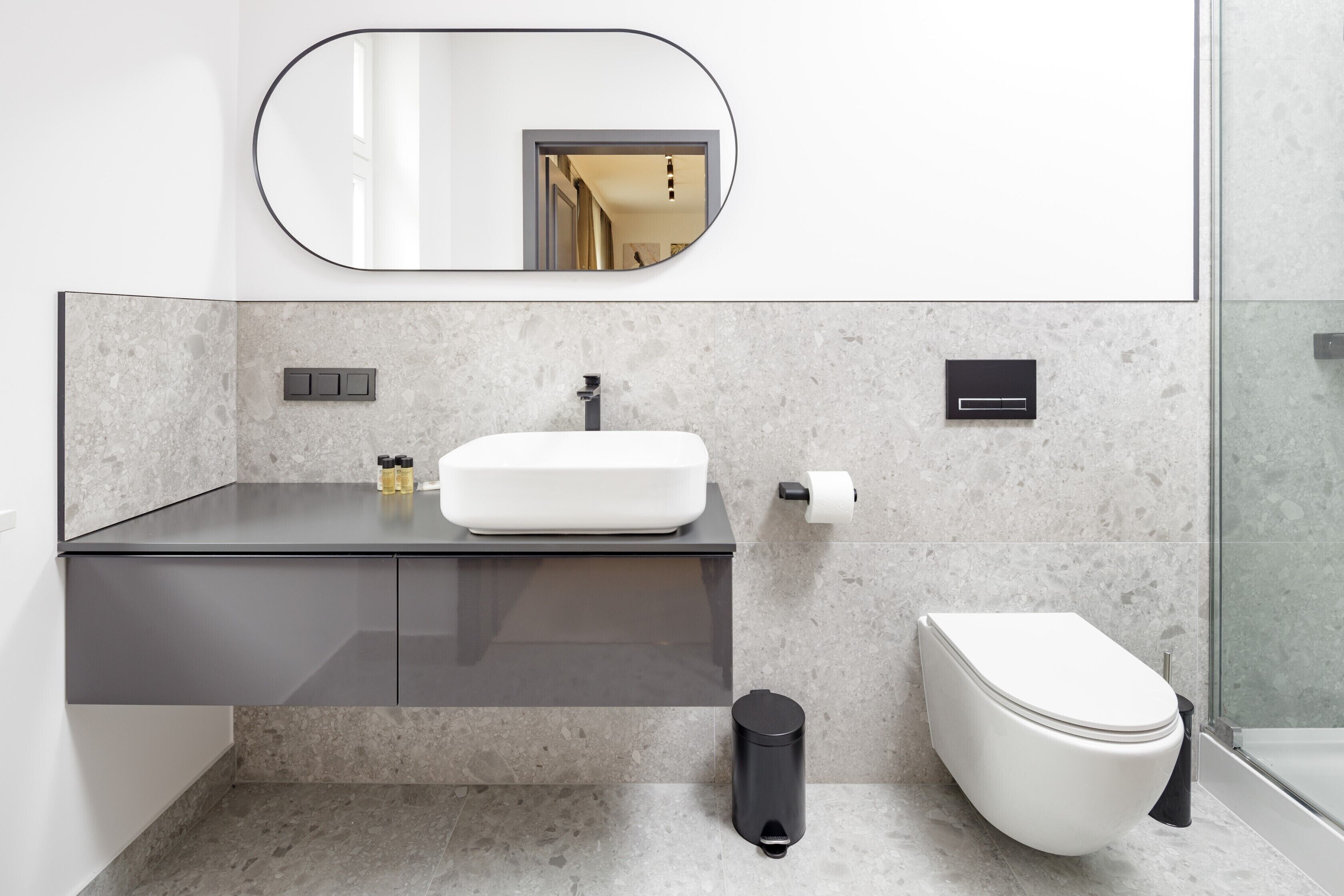 Ein modernes Badezimmer mit einem weißen Waschbecken, einem Spiegel, einer Toilette und einem Mülleimer.