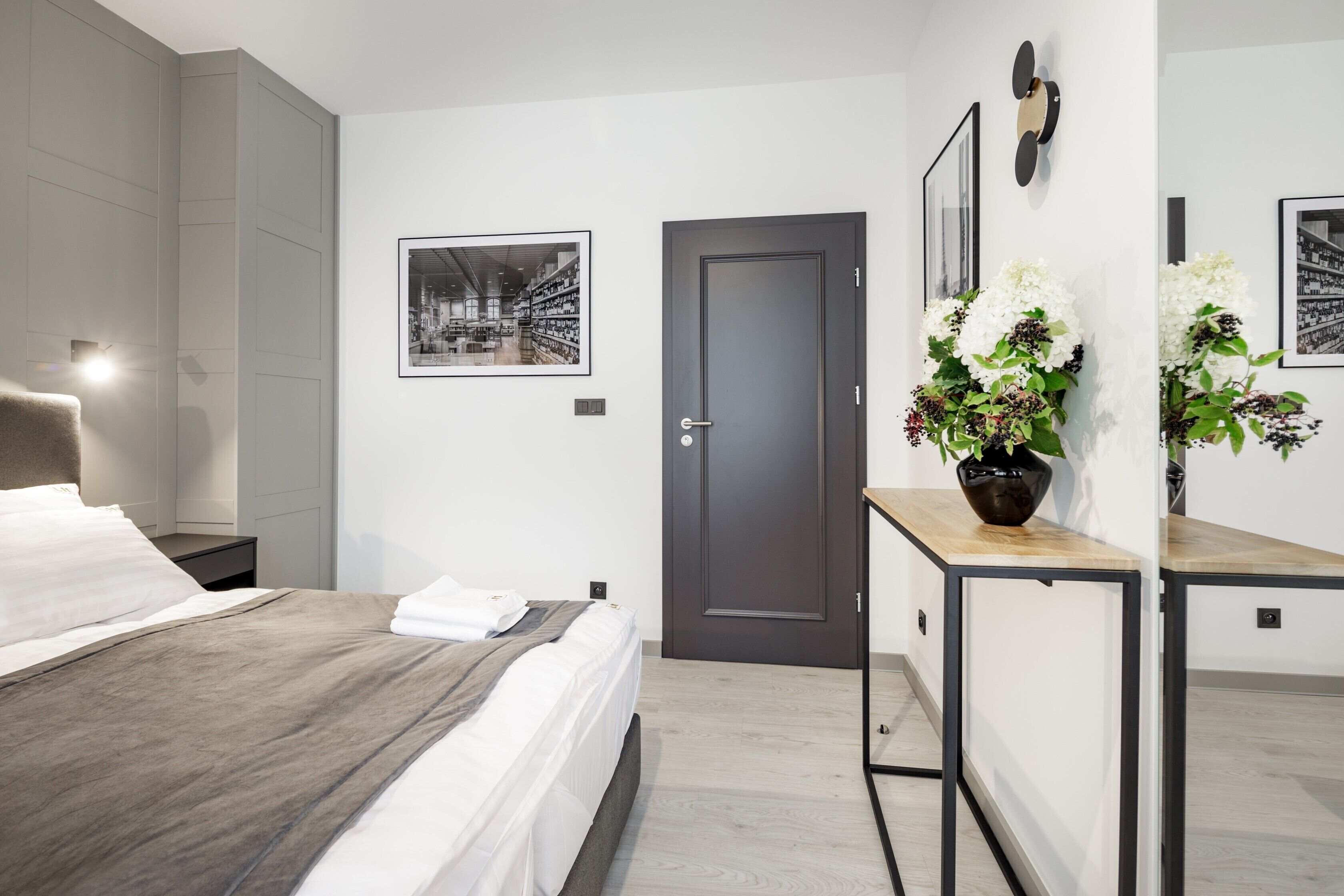 Quarto de hotel moderno com cama, mesa de cabeceira e escrivaninha com um vaso de flores.