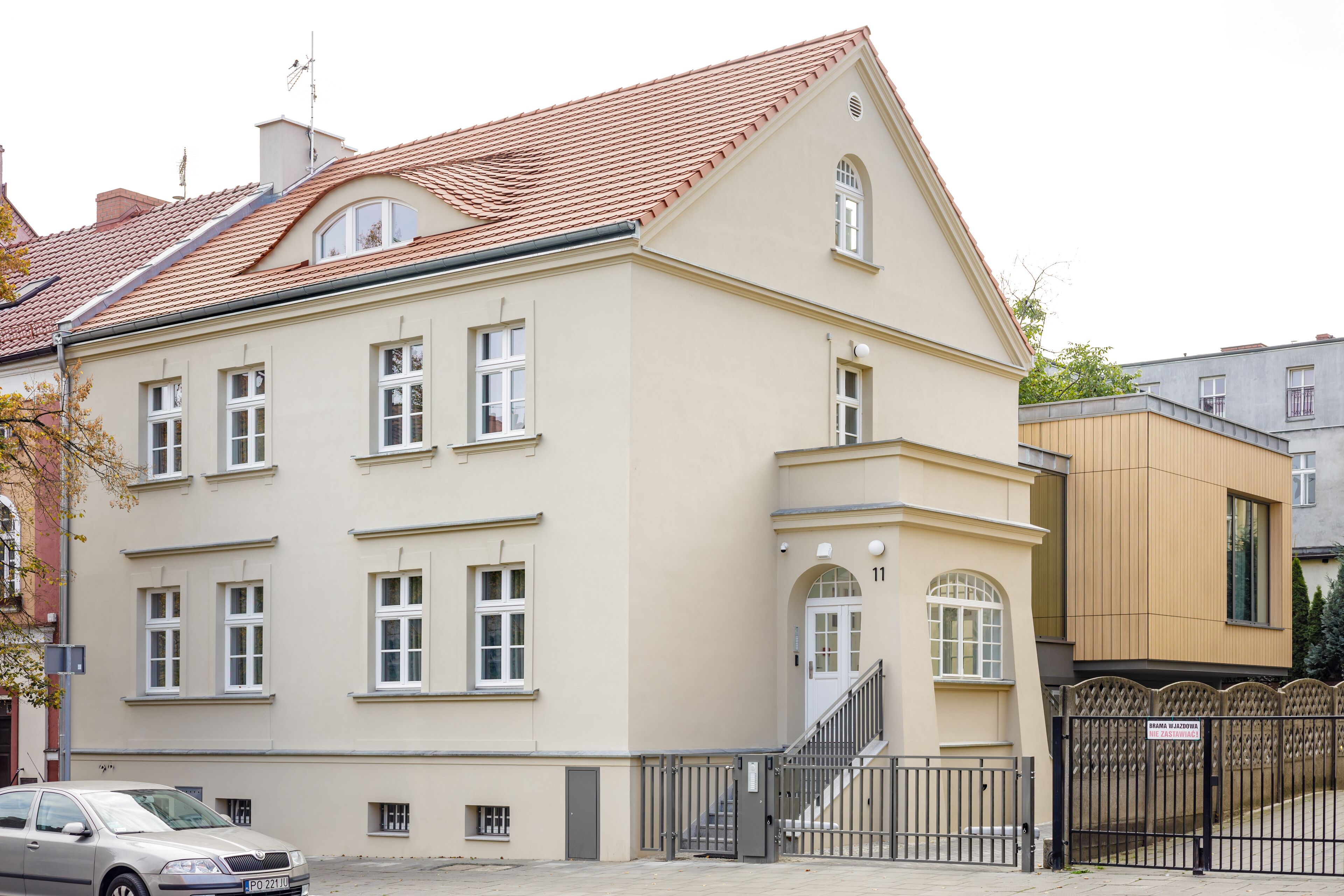 A two-story building with a beige facade, a red-tiled roof, and a black metal gate.