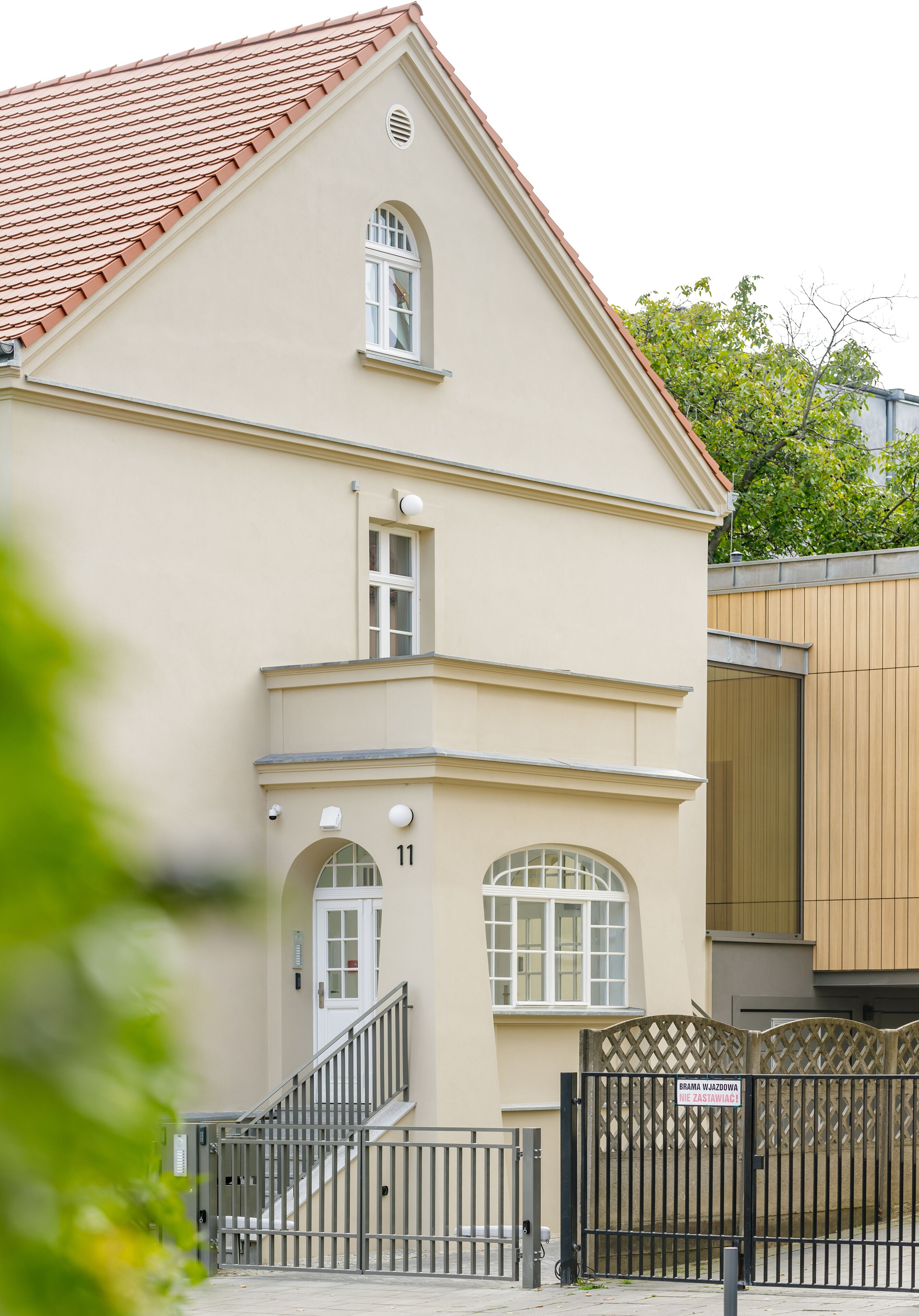 A two-story building with a beige facade, a red-tiled roof, and a black metal gate.