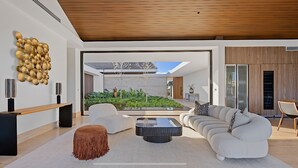 A modern living room with a sofa, coffee table, and ottoman, a wooden bench, and a wall art installation. - Srvittinivillas Flyvll/ Lux Spacious / Fam / Vacations / Casa de Campo Villas (La Romana)
